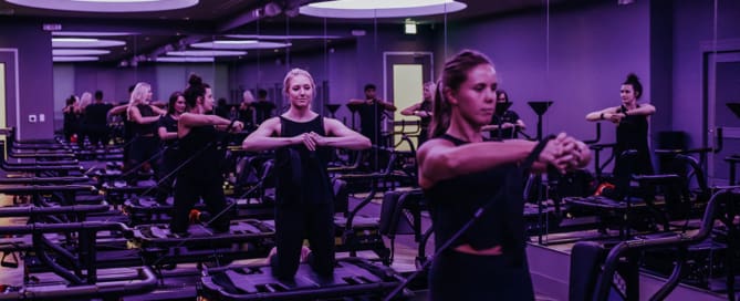 Group of women performing resistance exercises on Megaformer machines in a studio