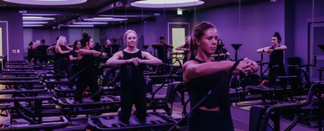 Group fitness class performing resistance exercises on Megaformer machines