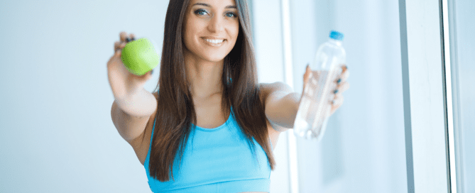 Woman holding a green apple and water bottle toward the camera