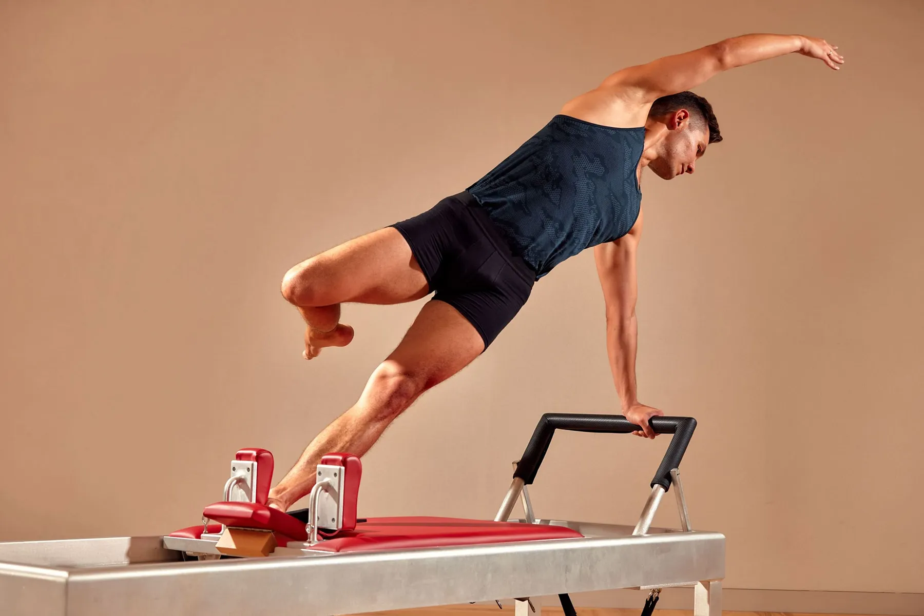 pilates-reformer-side-balance-male-instructor.tight-dallas. Man performing advanced side balance on a Pilates reformer machine