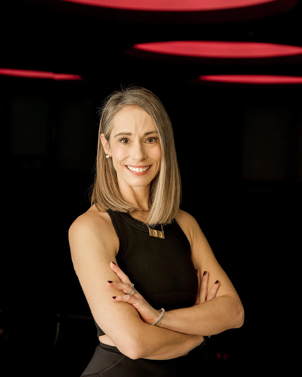 fitness-instructor-nicole-smiling-with-arms-crossed-in-modern-studio.tight-dallas. Fitness instructor Nicole smiling with arms crossed in a studio.