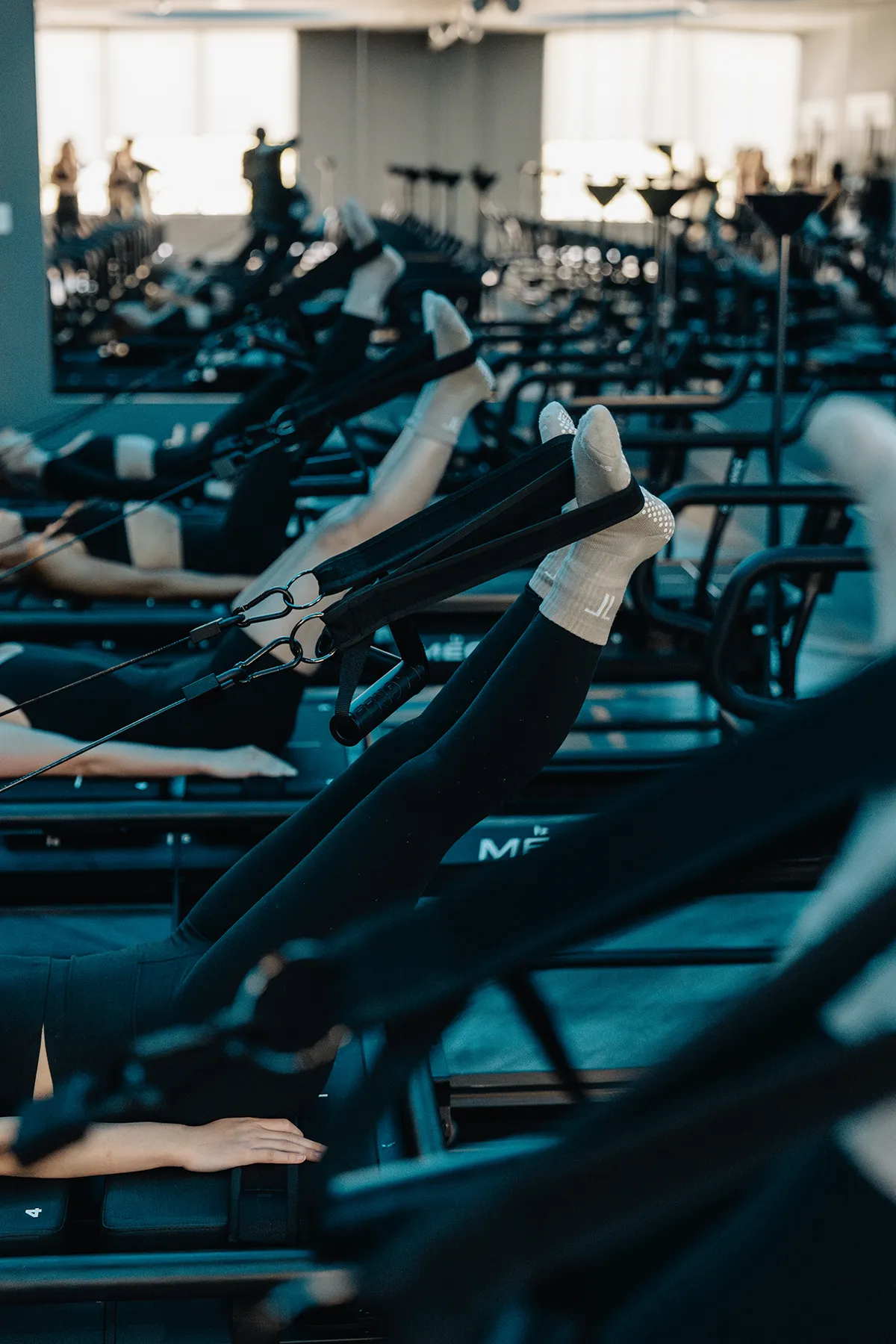 lagree-leg-workout-megaformer-tight-dallas Clients performing leg press exercise with straps on Megaformer machines at TIGHT Dallas.