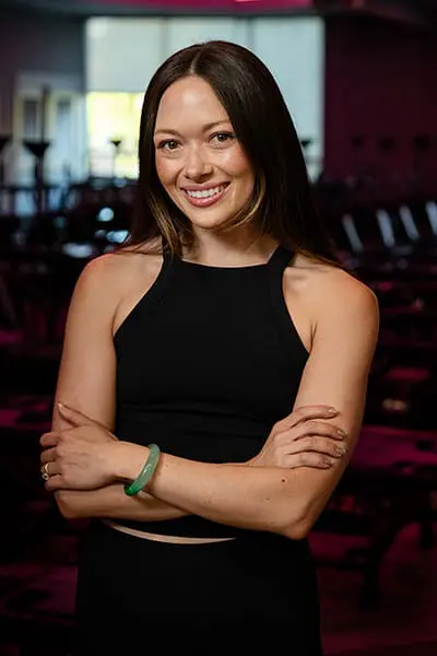 Fitness instructor Caiti smiling with arms crossed in a studio.