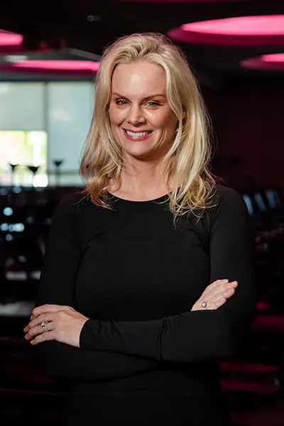 Fitness instructor Deirdre smiling with arms crossed in a studio.