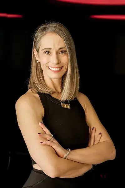 Fitness instructor Nicole smiling with arms crossed in a studio.