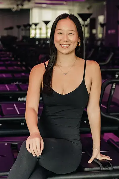 Fitness instructor Nina smiling while seated on a Megaformer machine in a studio.