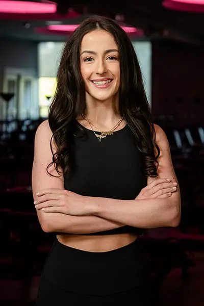 Fitness instructor Sydneigh smiling with arms crossed in a studio.