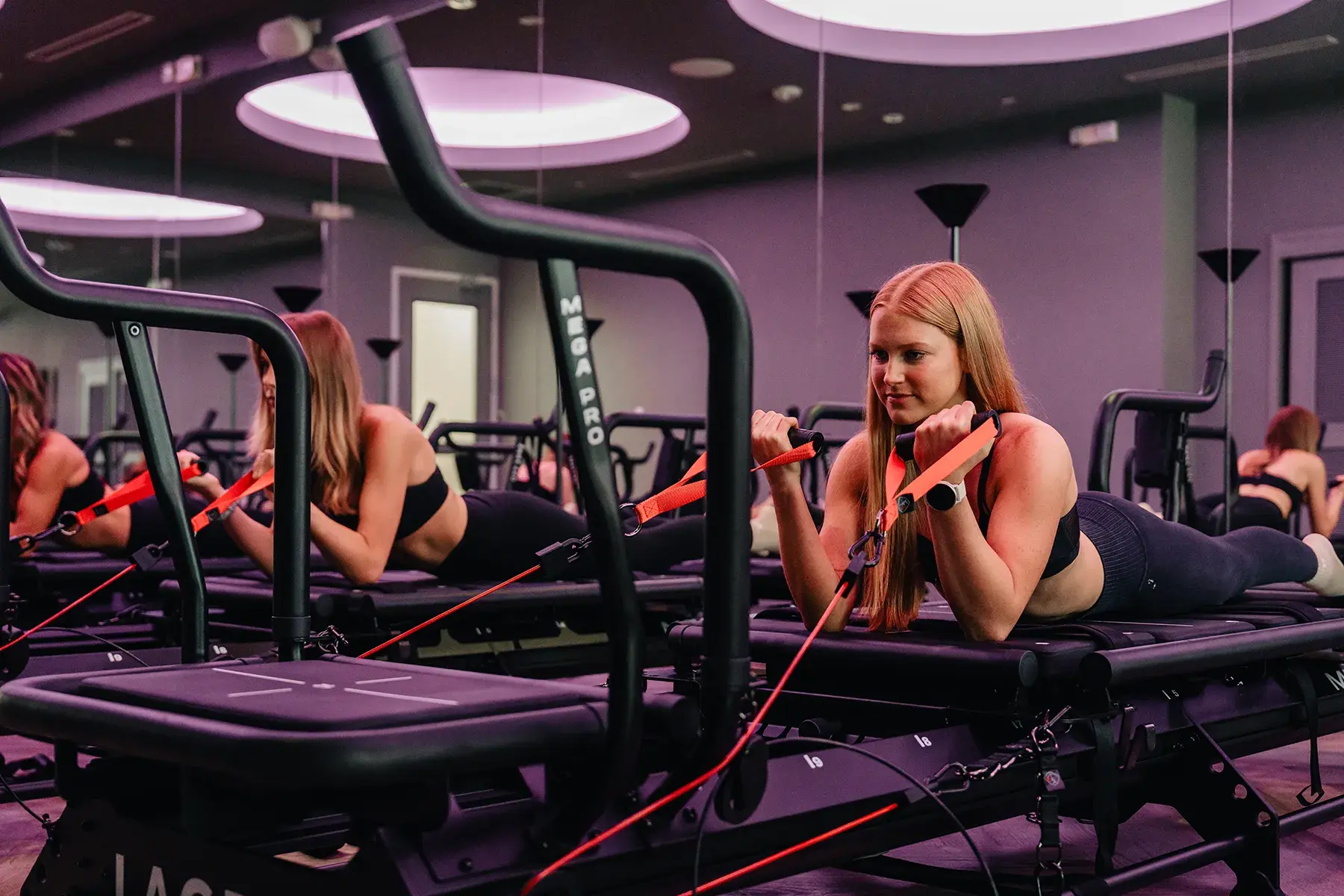 woman-performing-arm-resistance-exercise-on-megaformer-machine-in-fitness-studio.tight-dallas. Woman performing arm resistance exercise on a Megaformer machine in a fitness studio.