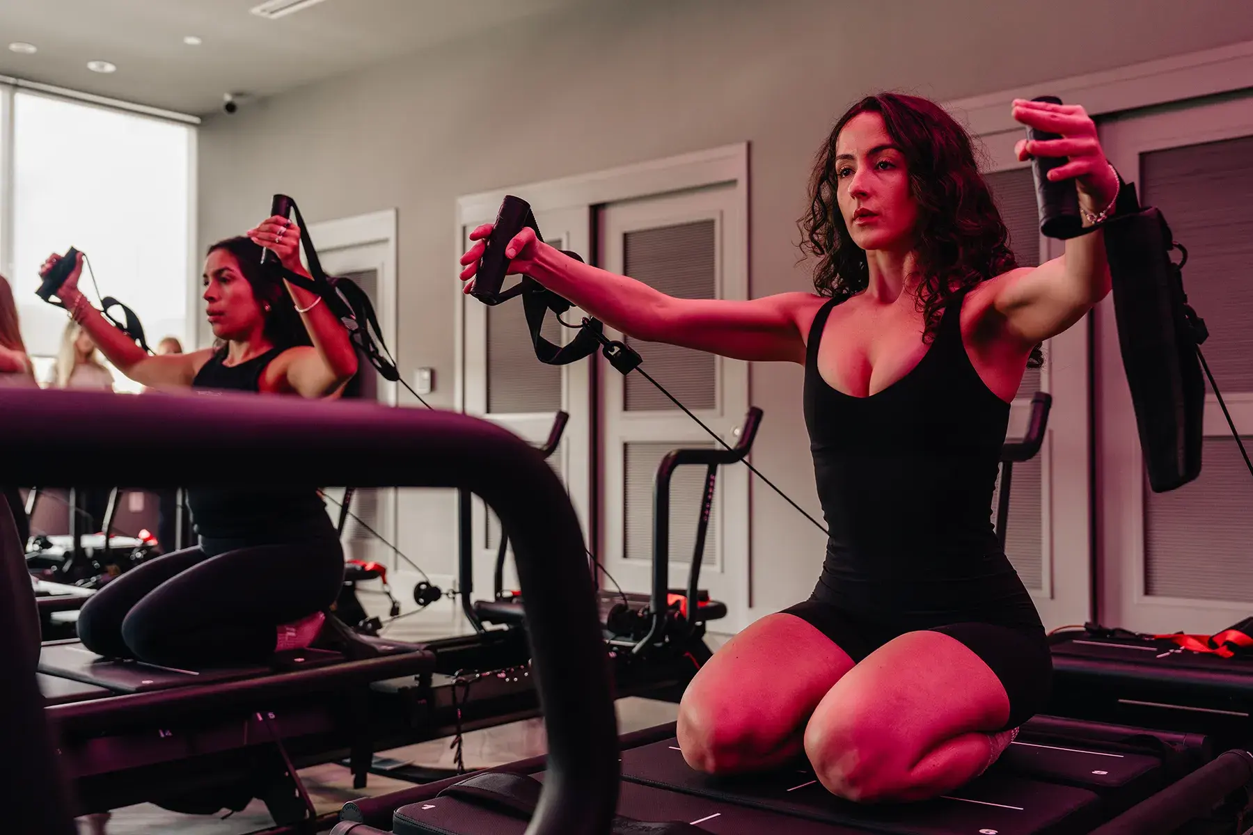 woman-performing-upper-body-resistance-exercise-on-megaformer-machine-in-studio.tight-dallas. Woman performing upper body resistance exercise on a Megaformer machine in a fitness studio.