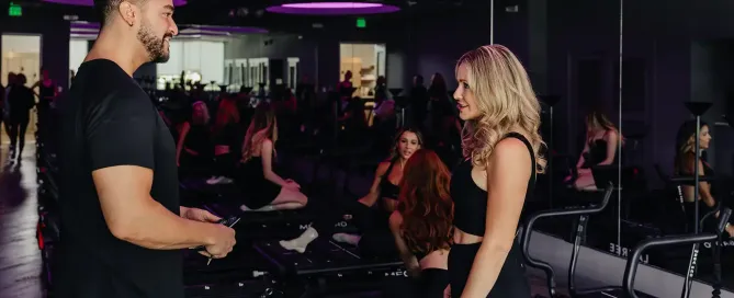 Two TIGHT Dallas instructors chatting between Megaformer machines in a purple-lit Lagree studio