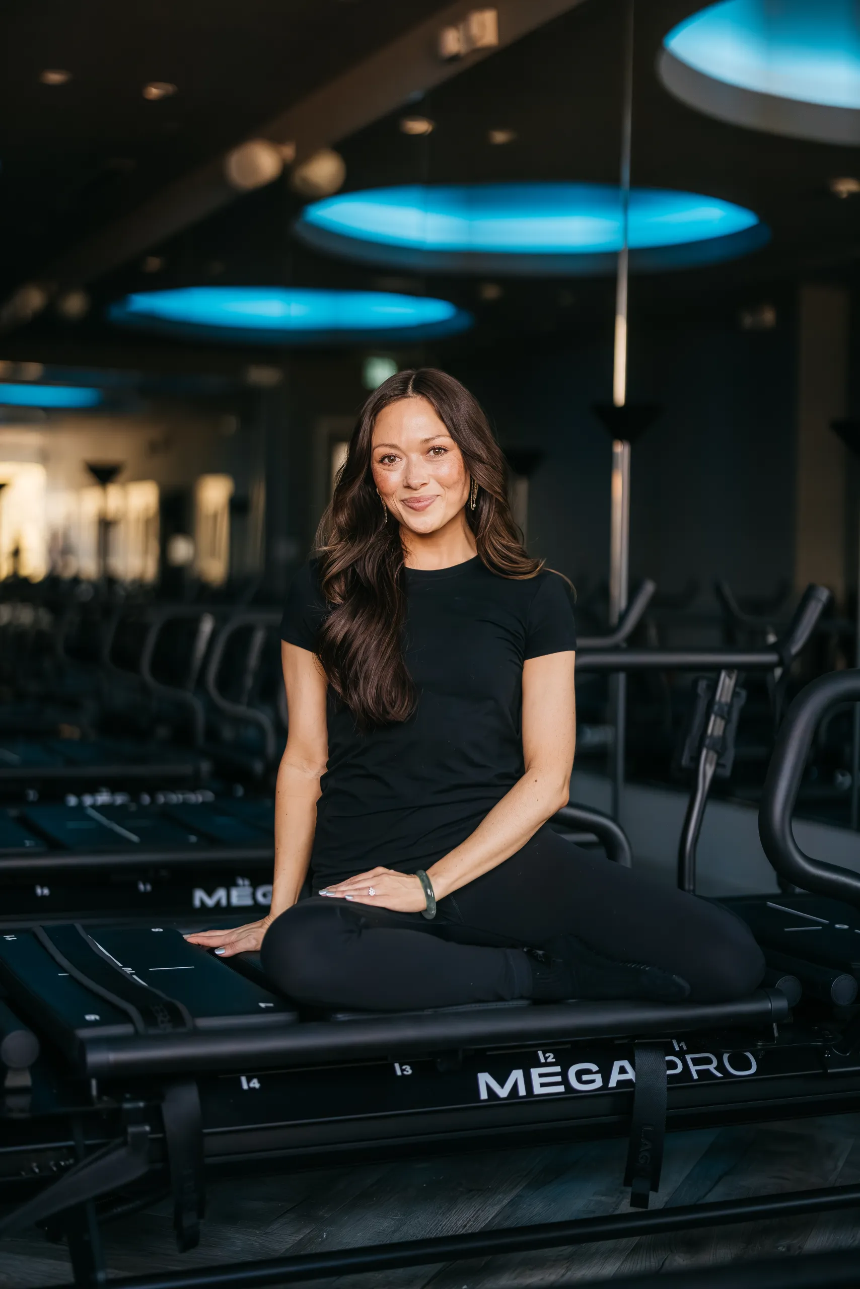 lagree-instructor-caiti-seated-on-megapro-machine-tight-dallas. Lagree instructor Caiti smiling while seated on a MegaPro machine at Tight Dallas
