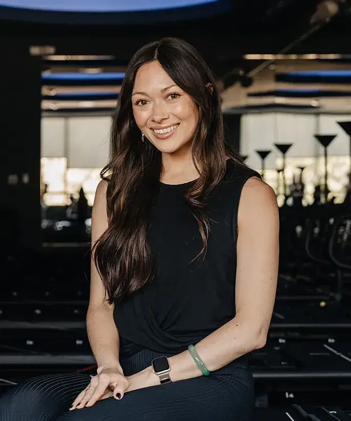 Fitness instructor Caiti Morris Hatton smiling while seated in a studio.