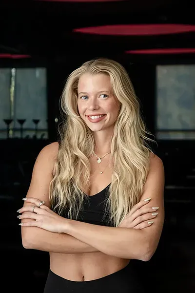 Fitness instructor Peyton smiling with arms crossed in a studio.